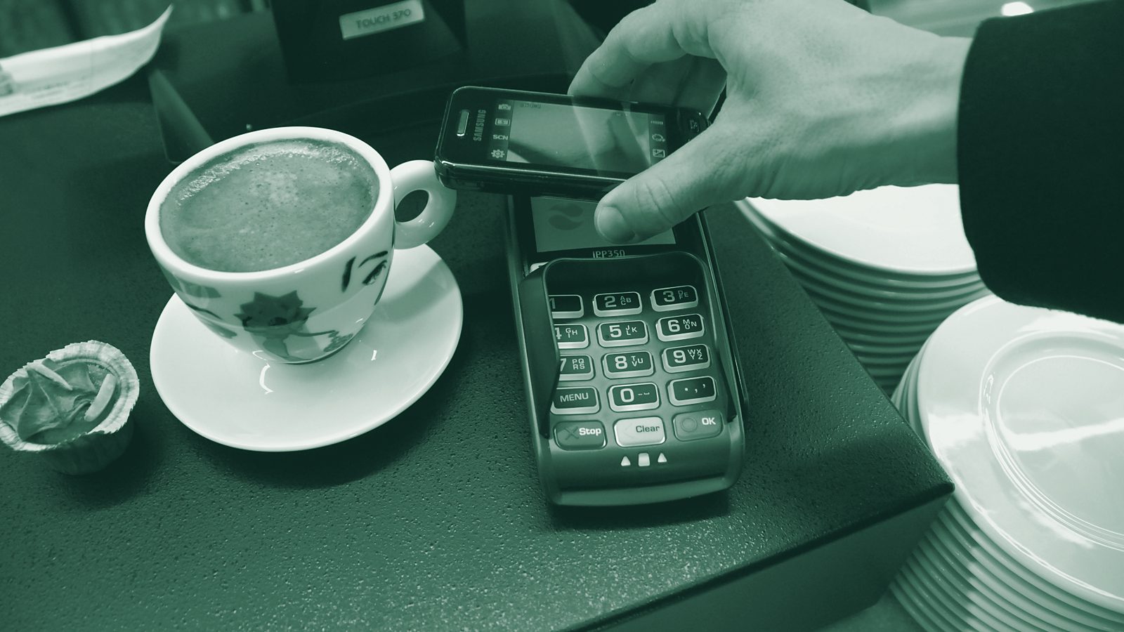 A smartphone held over a card payment terminal beside a cup of coffee
