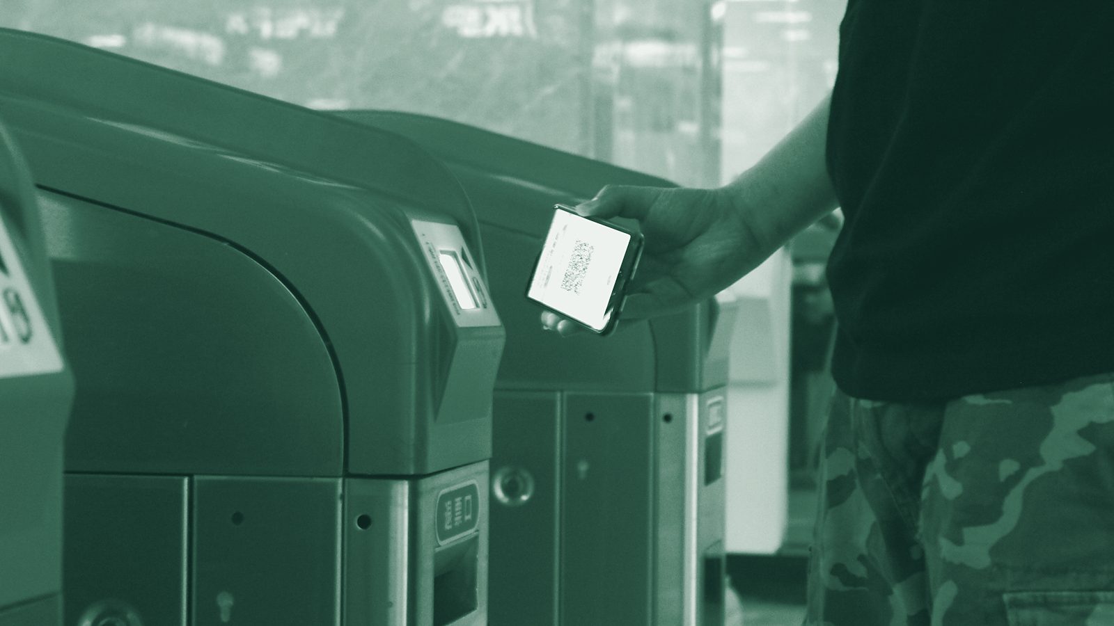 A passenger holding a phone with a QR code up to a metro ticket gate