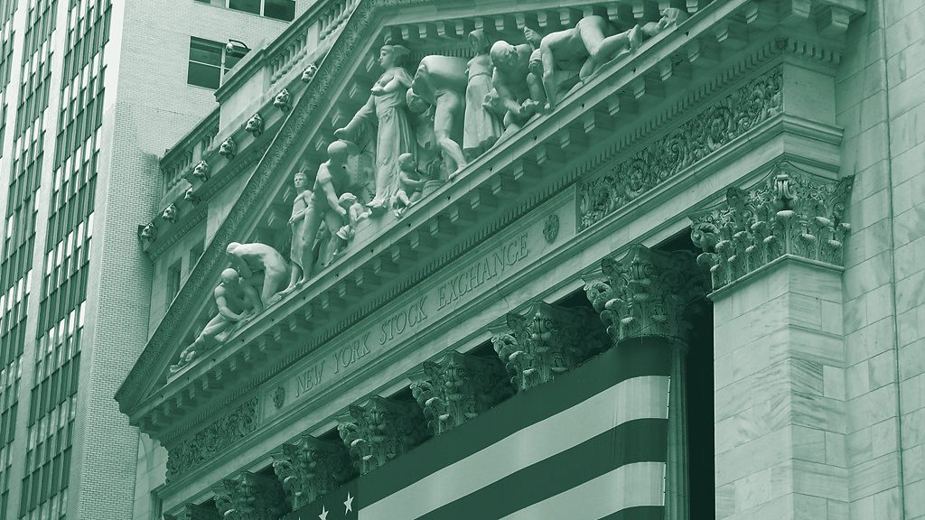 The carved pediment and columns of the New York Stock Exchange building with a large US flag