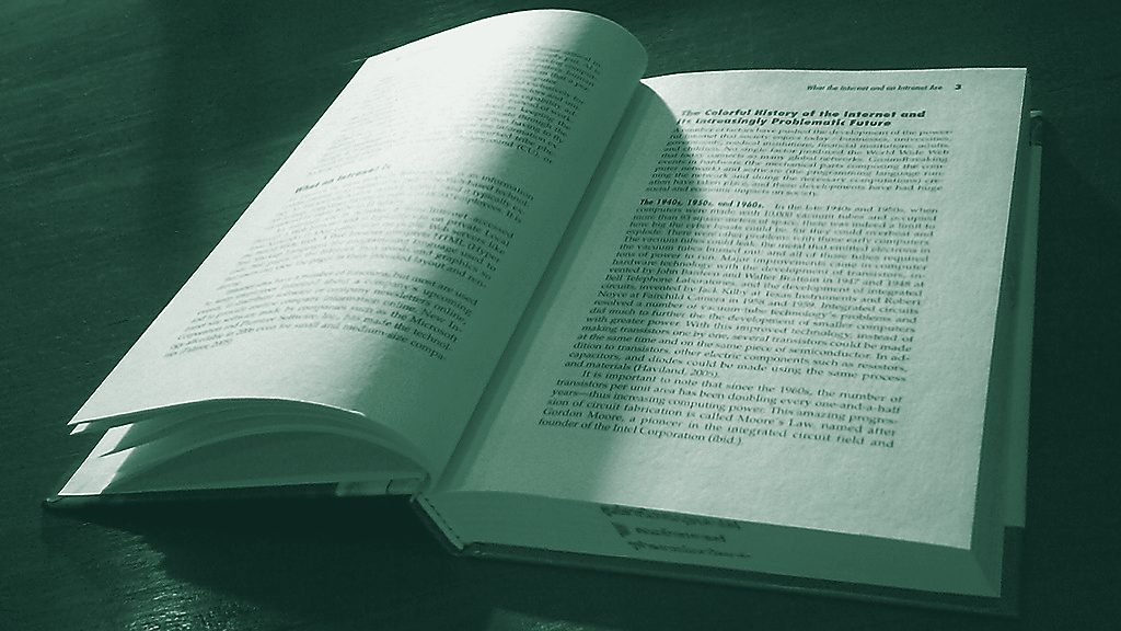 An open hardback book lying on a dark table