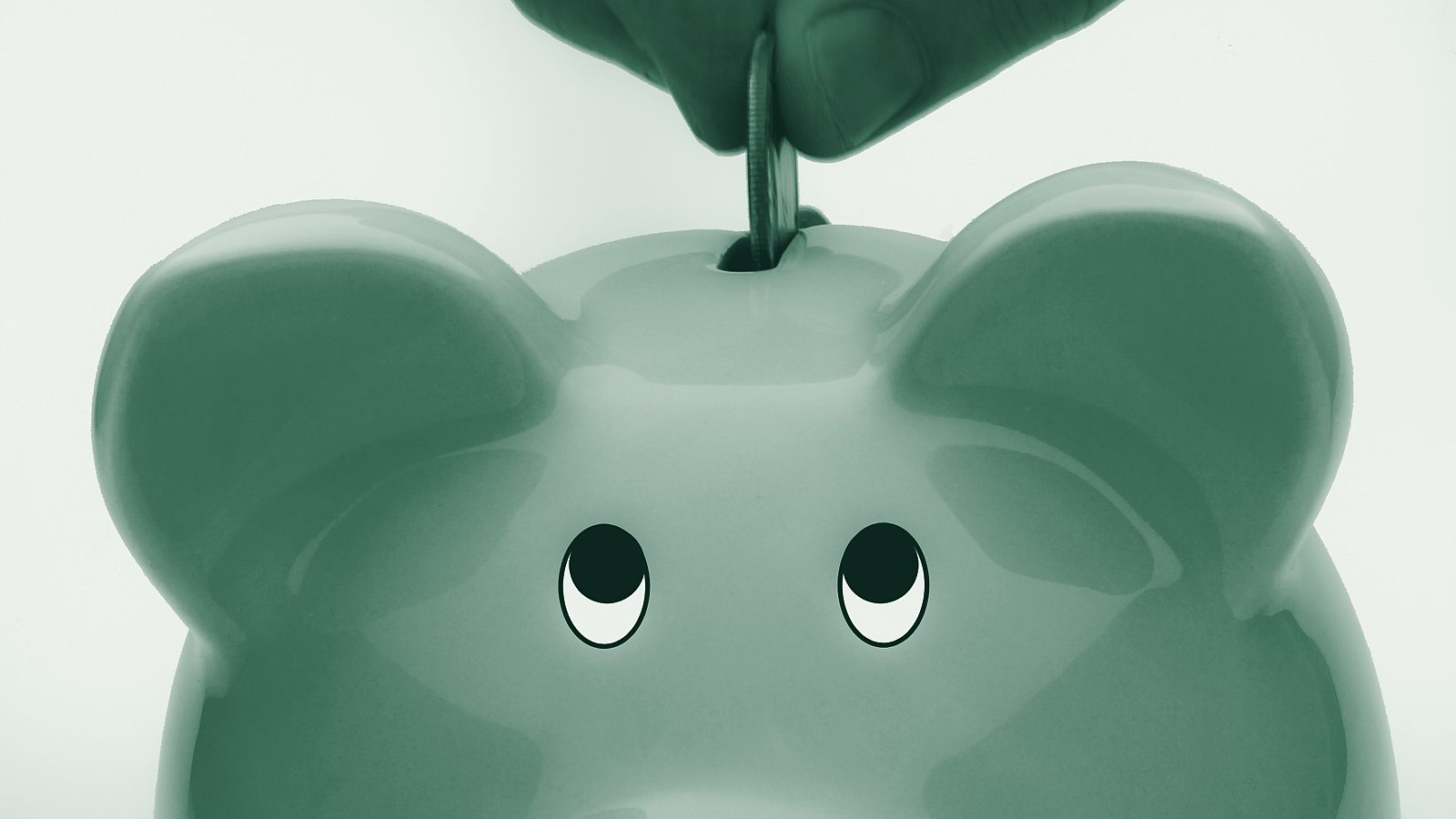 A hand dropping a coin into a pink piggy bank