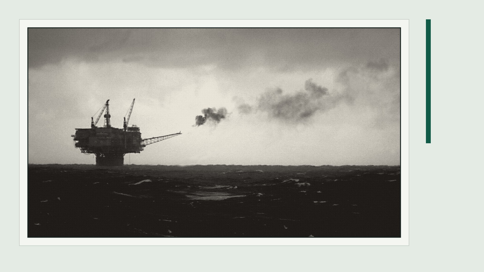 Black-and-white photo of an offshore oil platform flaring gas on a rough grey sea, framed on a pale green-grey mat with a green rule